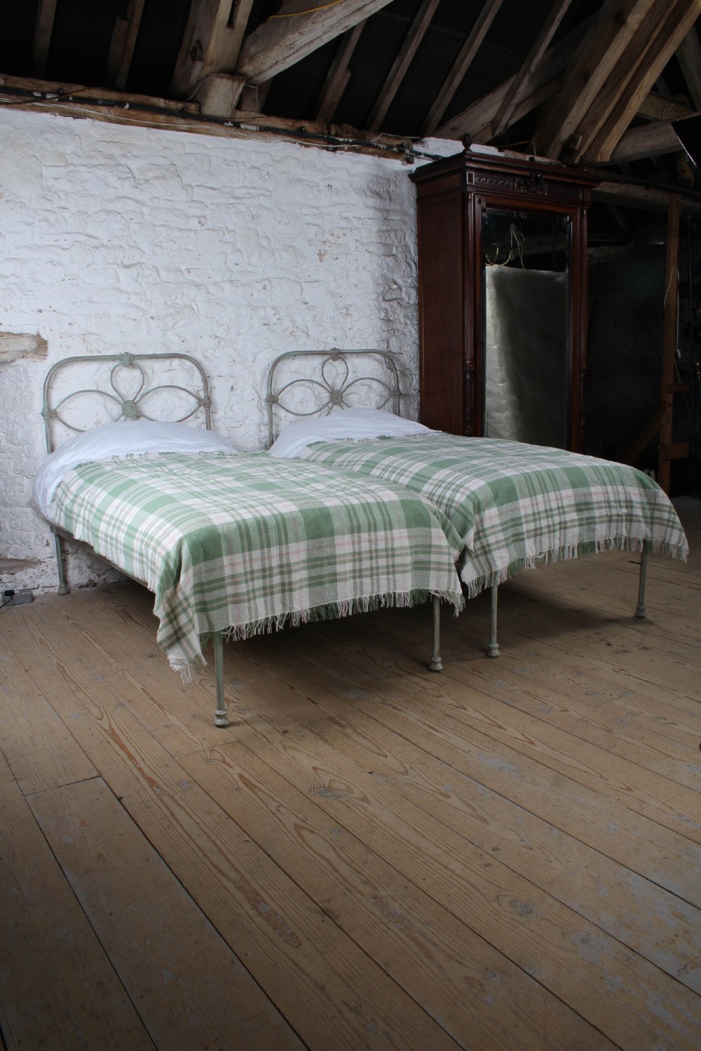 A pair of antique single iron bed frames featuring curved Celtic loop motifs on the headboards and a distressed painted finish.