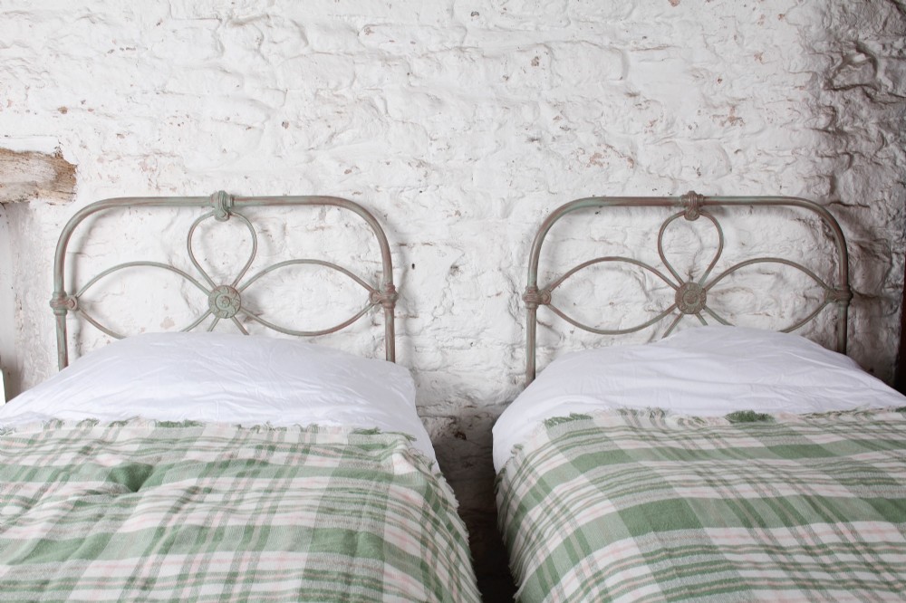 A pair of antique single iron bed frames featuring curved Celtic loop motifs on the headboards and a distressed painted finish. View II