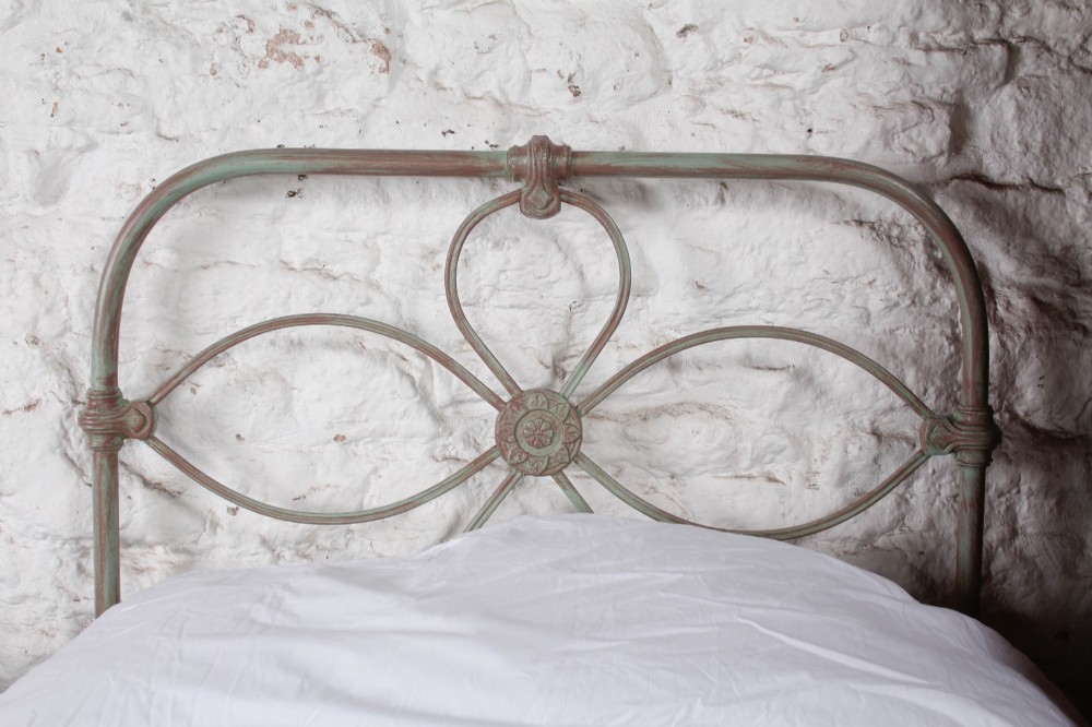 A pair of antique single iron bed frames featuring curved Celtic loop motifs on the headboards and a distressed painted finish. View IV