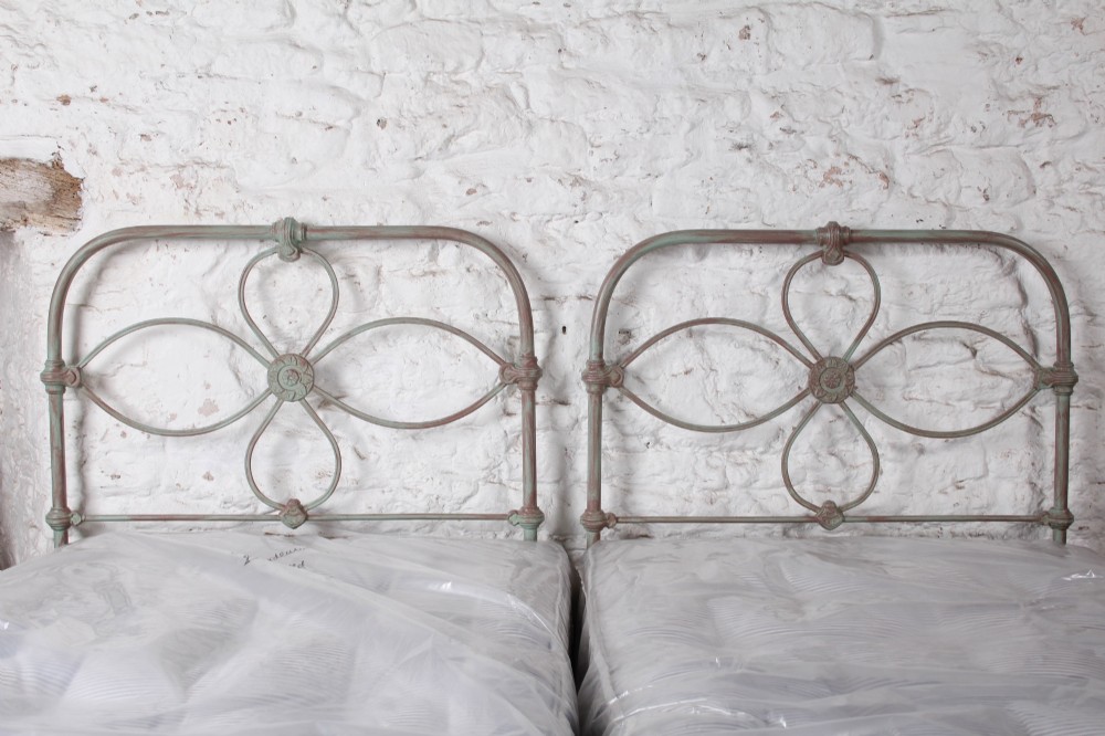 A pair of antique single iron bed frames featuring curved Celtic loop motifs on the headboards and a distressed painted finish. View VII