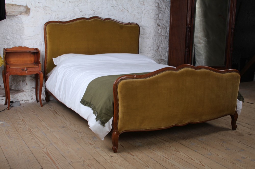 A French double bed frame crafted with a contoured dark wood border, olive velvet upholstery, brass stud trim, and cabriole legs.
