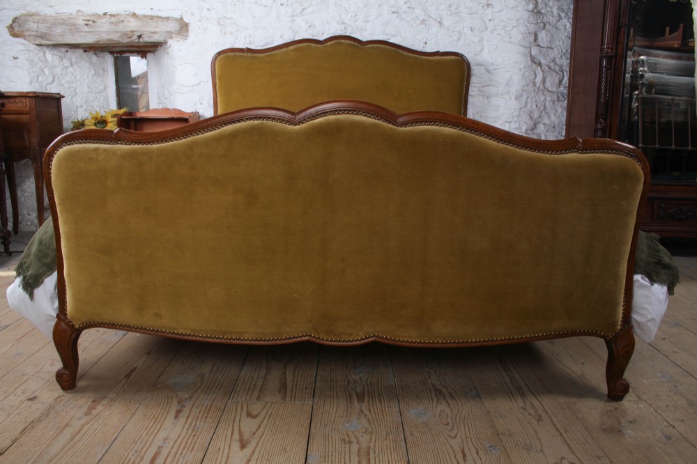 A French double bed frame crafted with a contoured dark wood border, olive velvet upholstery, brass stud trim, and cabriole legs. View III