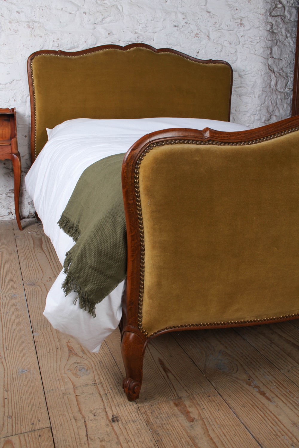 A French double bed frame crafted with a contoured dark wood border, olive velvet upholstery, brass stud trim, and cabriole legs. View IV