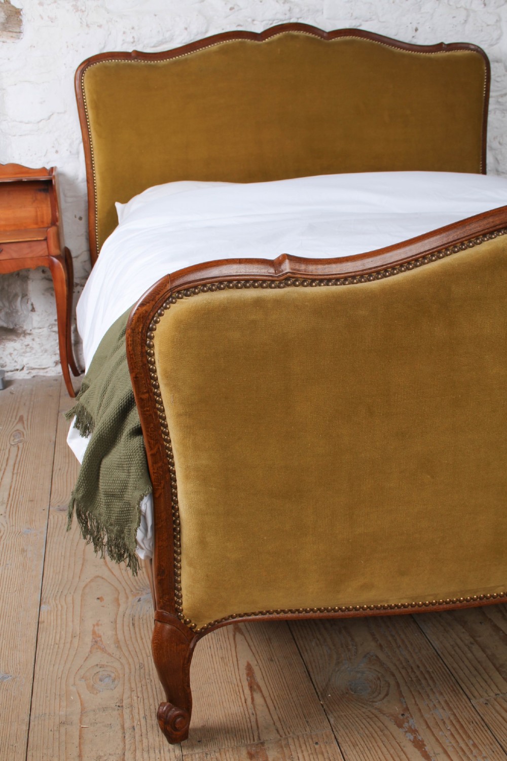 A French double bed frame crafted with a contoured dark wood border, olive velvet upholstery, brass stud trim, and cabriole legs. View VI