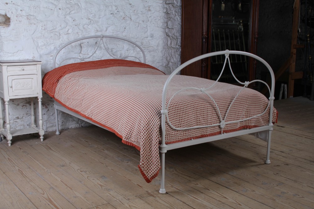 An off-white painted iron bedstead featuring a curved headboard and footboard with Celtic-style decorative metal scrollwork.