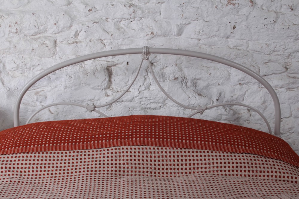 An off-white painted iron bedstead featuring a curved headboard and footboard with Celtic-style decorative metal scrollwork. View VII