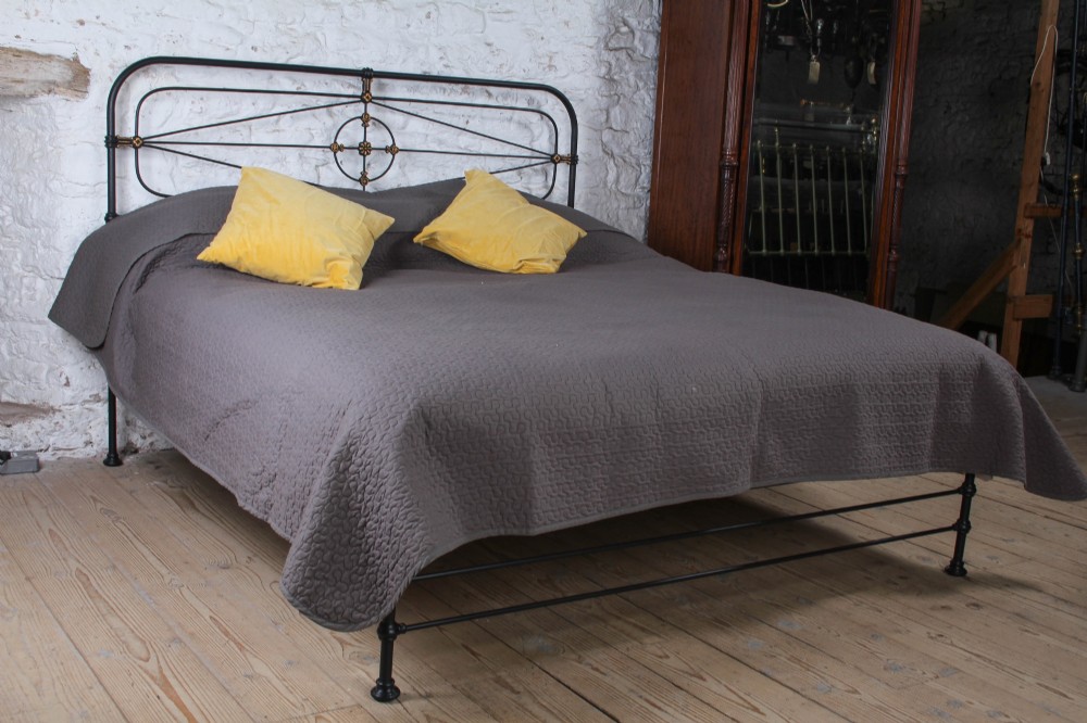 A Victorian super king black iron bed frame featuring geometric rod work and central brass highlights on the headboard.