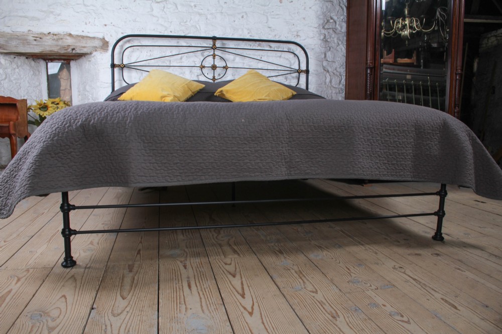 A Victorian super king black iron bed frame featuring geometric rod work and central brass highlights on the headboard. View VI
