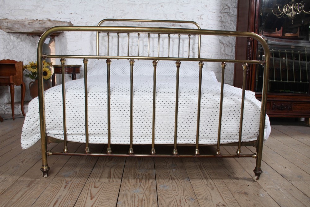 An antique French all-brass double bed frame featuring a rounded headboard and footboard with slender vertical spindles set on castor wheels. View III