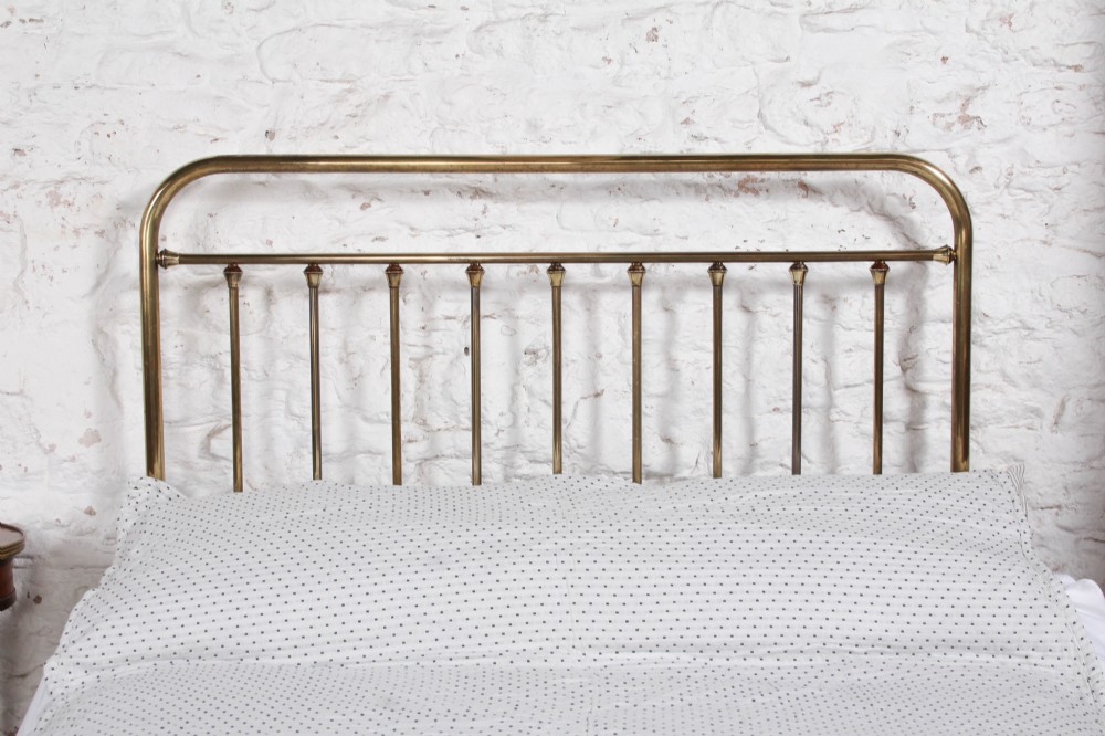 An antique French all-brass double bed frame featuring a rounded headboard and footboard with slender vertical spindles set on castor wheels. View V