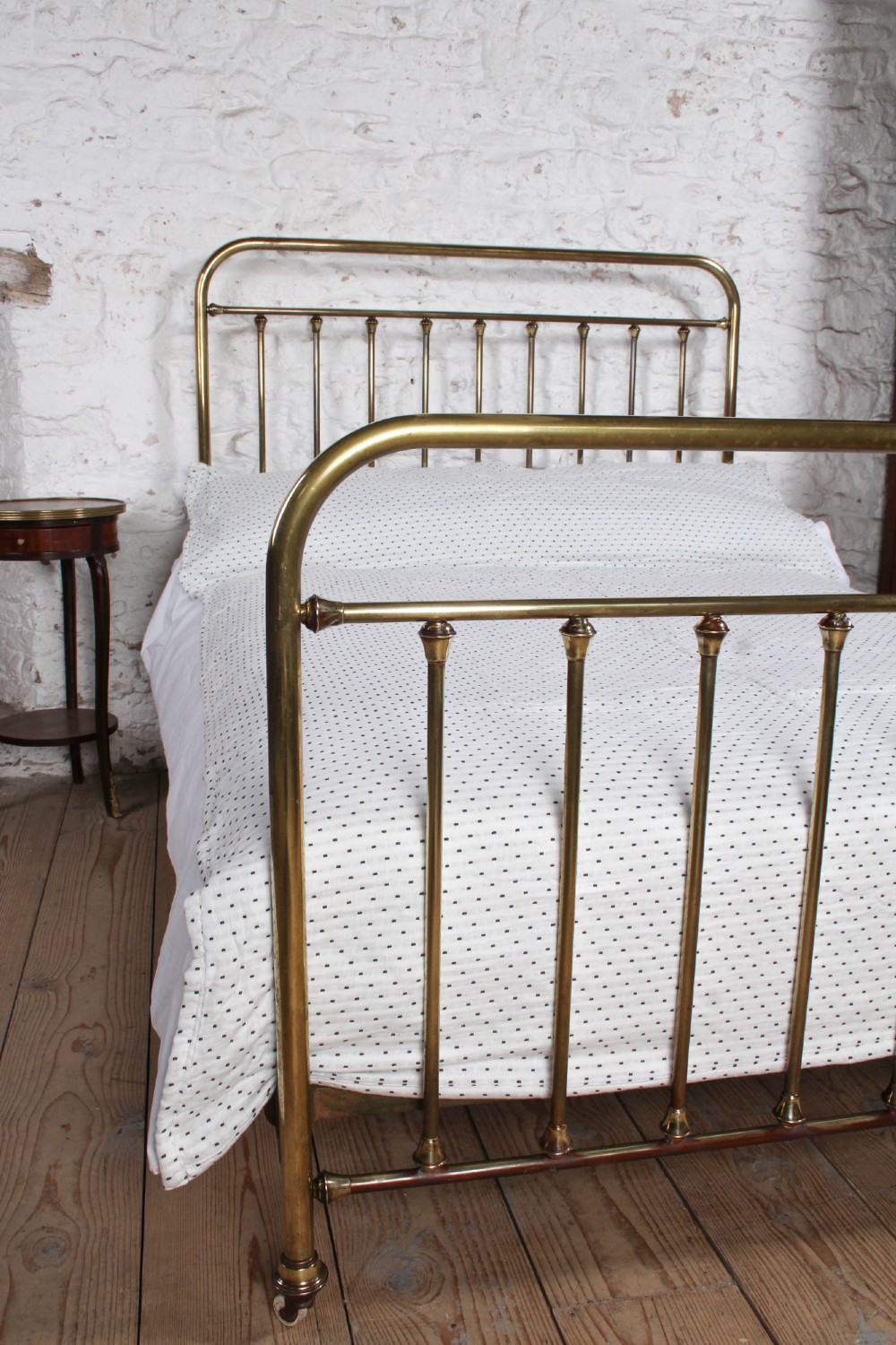 An antique French all-brass double bed frame featuring a rounded headboard and footboard with slender vertical spindles set on castor wheels. View VII