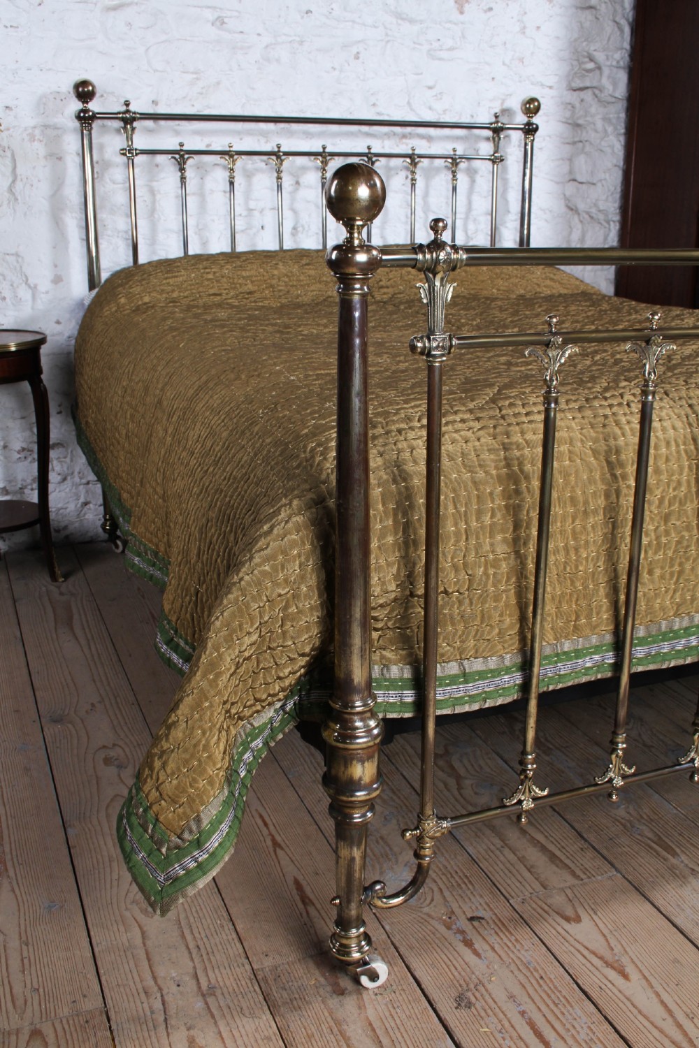 An antique Victorian brass king-size bedstead featuring vertical tubular spindles, decorative cast connectors, top rail ball finials, and original white ceramic castors. View II