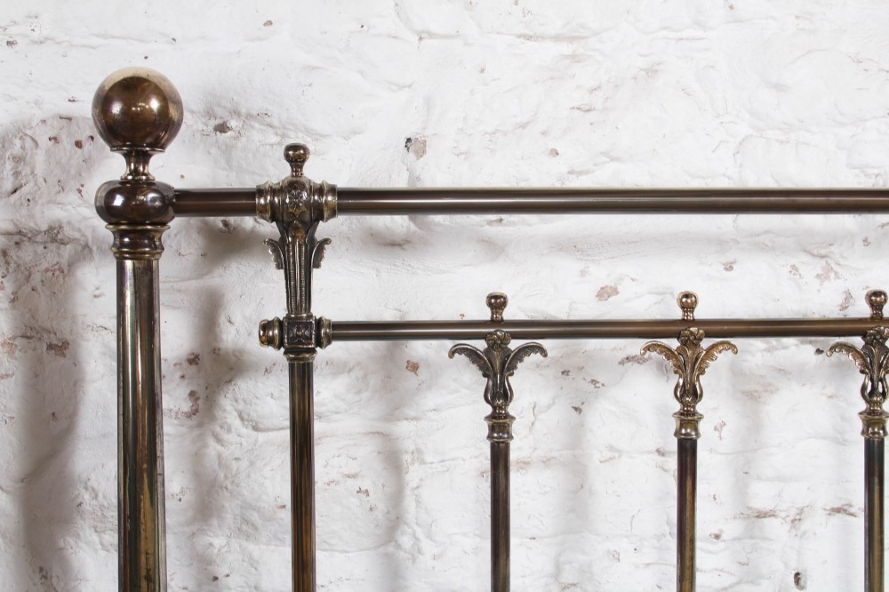 An antique Victorian brass king-size bedstead featuring vertical tubular spindles, decorative cast connectors, top rail ball finials, and original white ceramic castors. View XI