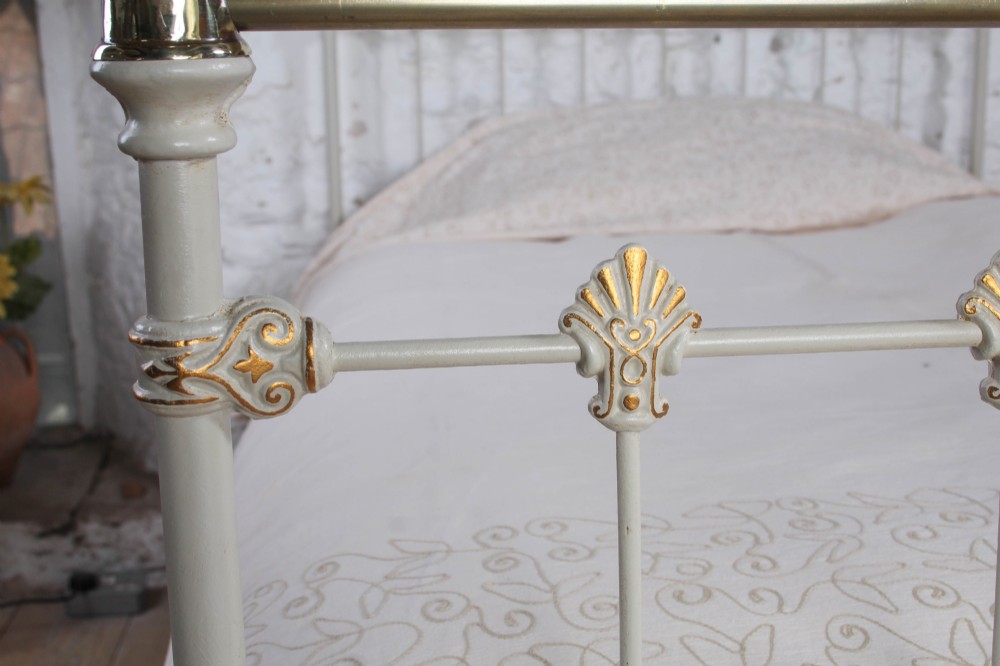 A Victorian cream-painted iron and brass three-quarter bedstead featuring vertical spindles, decorative cast motifs, and polished brass top rails with spherical finials. View VII