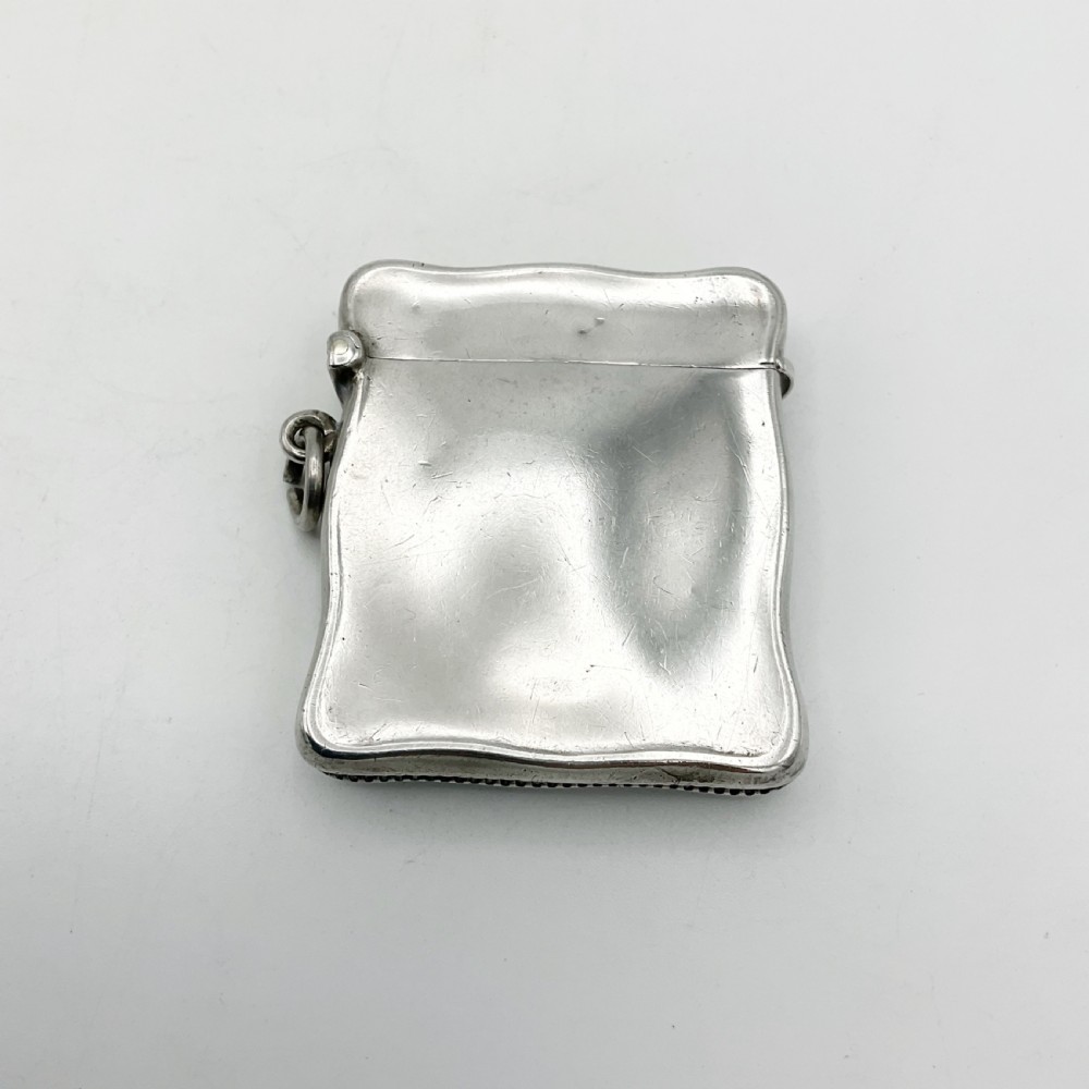 An Edwardian sterling silver vesta case with a contoured rectangular shape, side suspension ring, and hinged lid.