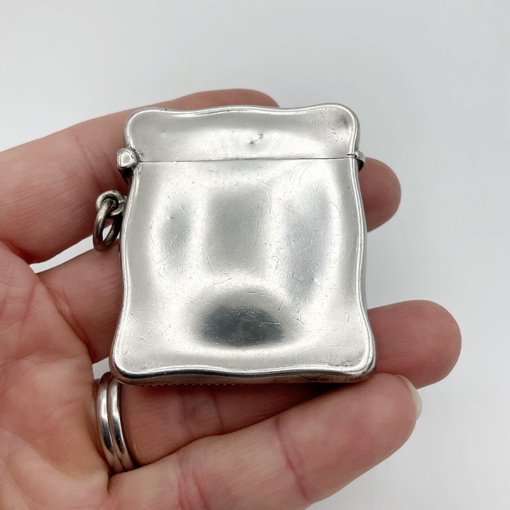 An Edwardian sterling silver vesta case with a contoured rectangular shape, side suspension ring, and hinged lid. View VI
