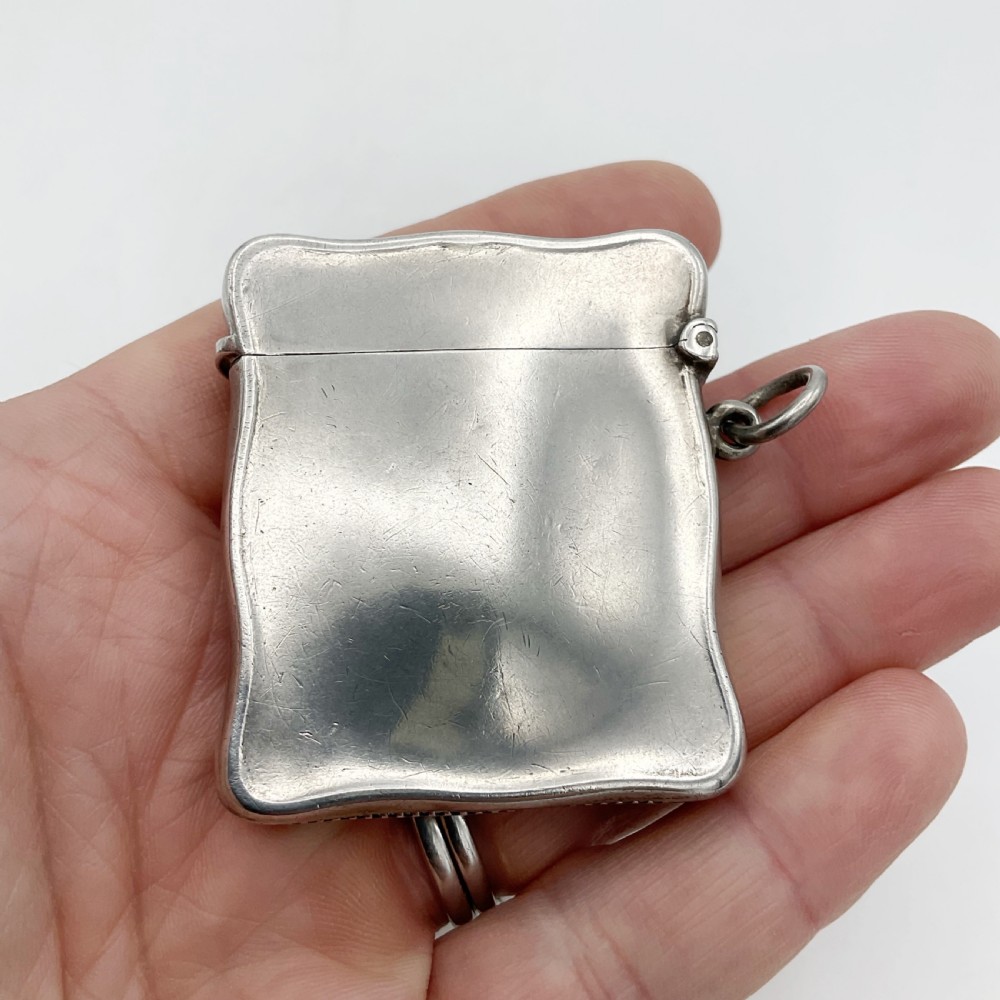 An Edwardian sterling silver vesta case with a contoured rectangular shape, side suspension ring, and hinged lid. View VII