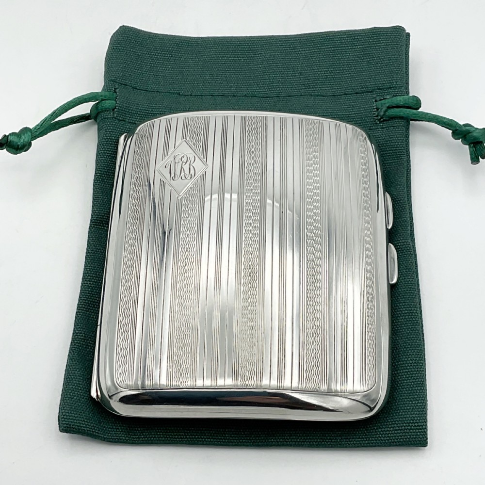 A curved rectangular sterling silver case featuring linear engine-turned pattern work and an engraved diamond monogram cartouche.