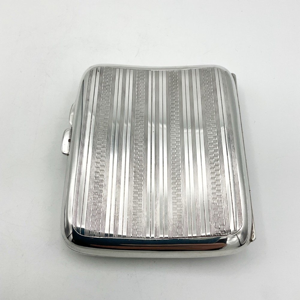 A curved rectangular sterling silver case featuring linear engine-turned pattern work and an engraved diamond monogram cartouche. View V