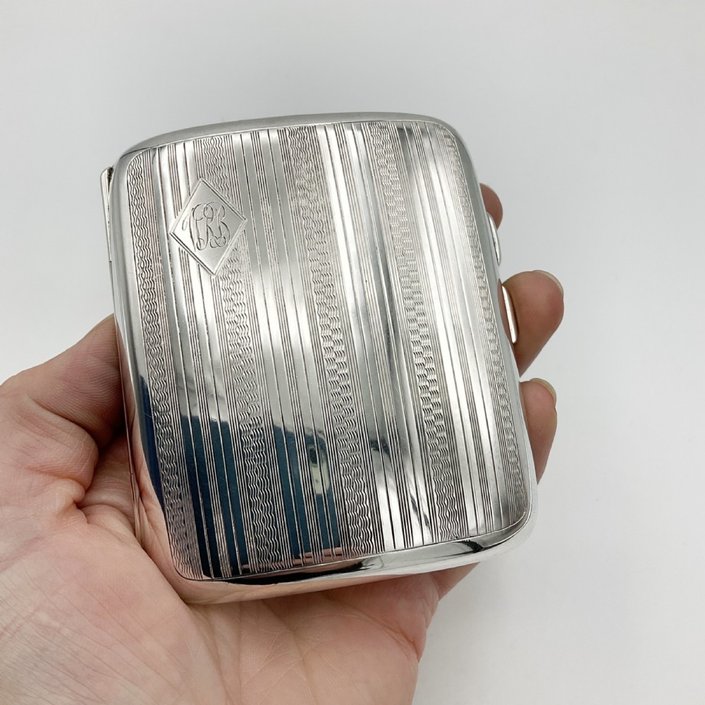 A curved rectangular sterling silver case featuring linear engine-turned pattern work and an engraved diamond monogram cartouche. View VI