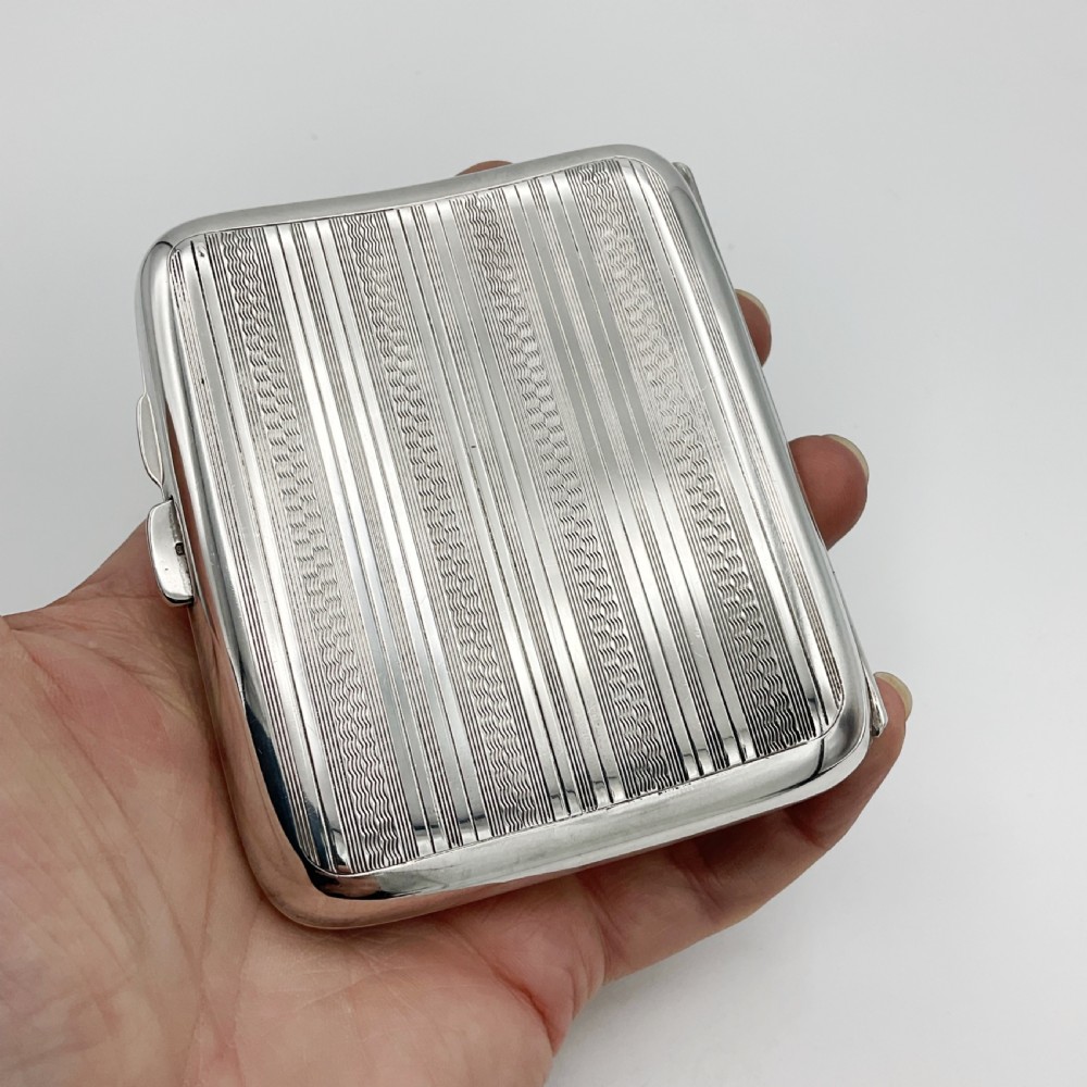 A curved rectangular sterling silver case featuring linear engine-turned pattern work and an engraved diamond monogram cartouche. View VII