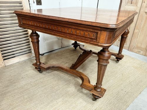fig 1. An antique French fruitwood dining table featuring turned legs, a carved apron, a low stretcher base, and small metal castors.