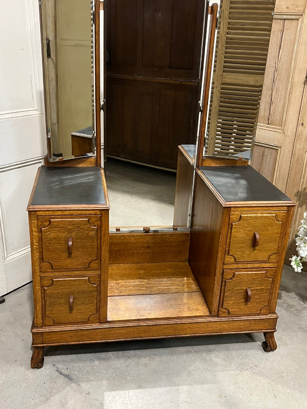 An Edwardian oak dressing table with a central full-length mirror flanked by two adjustable side mirrors, set above twin pedestal drawer units with carved detailing.