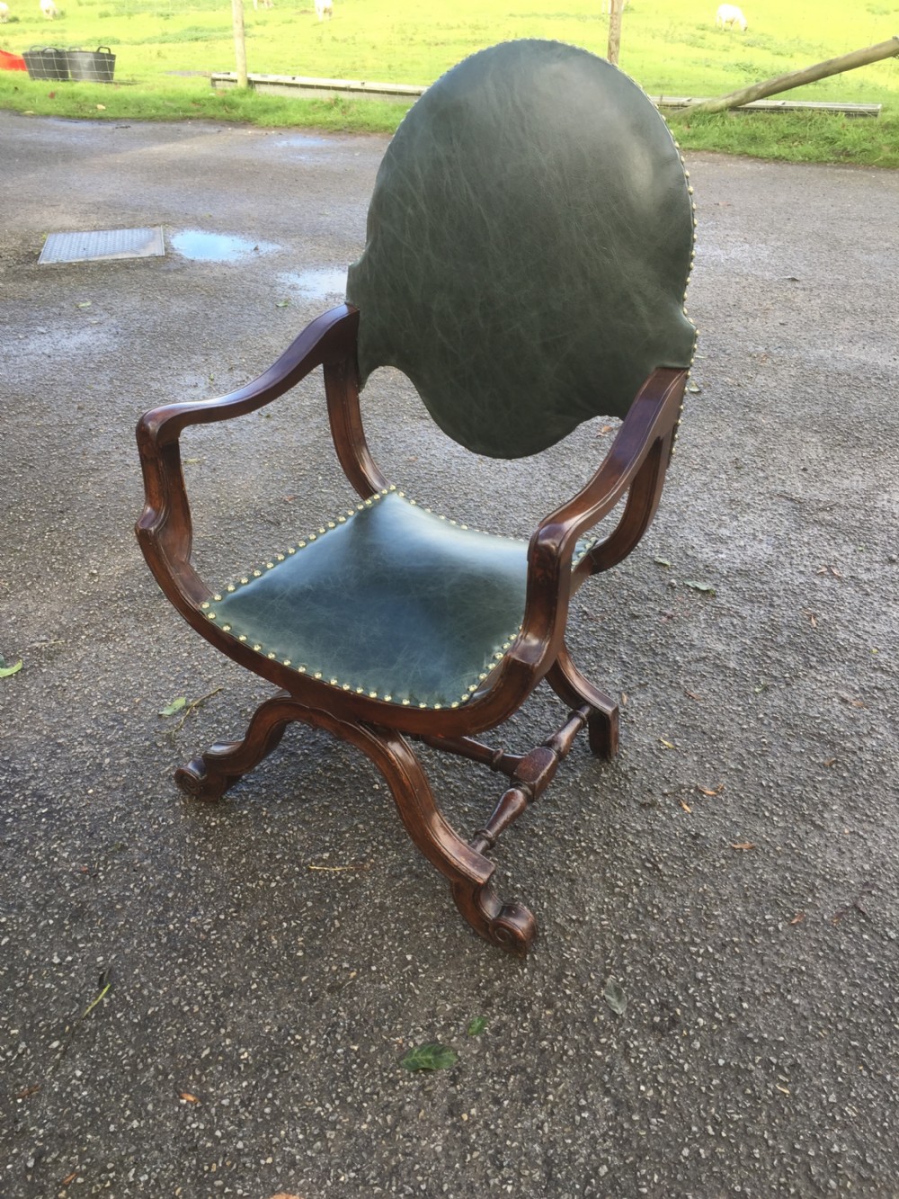 A nineteenth-century carved walnut X-frame armchair upholstered in dark olive green leather with brass stud details.