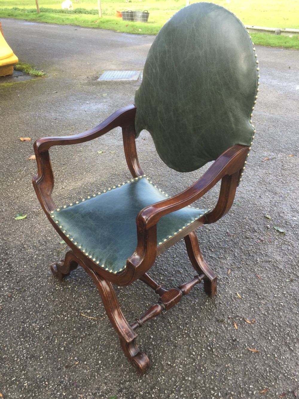 A nineteenth-century carved walnut X-frame armchair upholstered in dark olive green leather with brass stud details. View II
