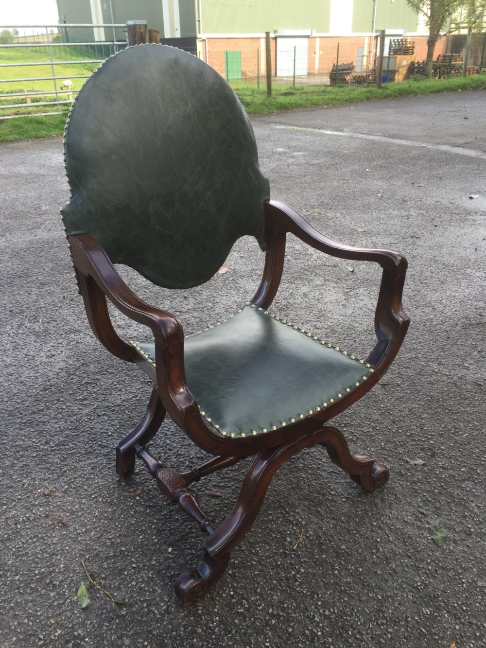 A nineteenth-century carved walnut X-frame armchair upholstered in dark olive green leather with brass stud details. View III