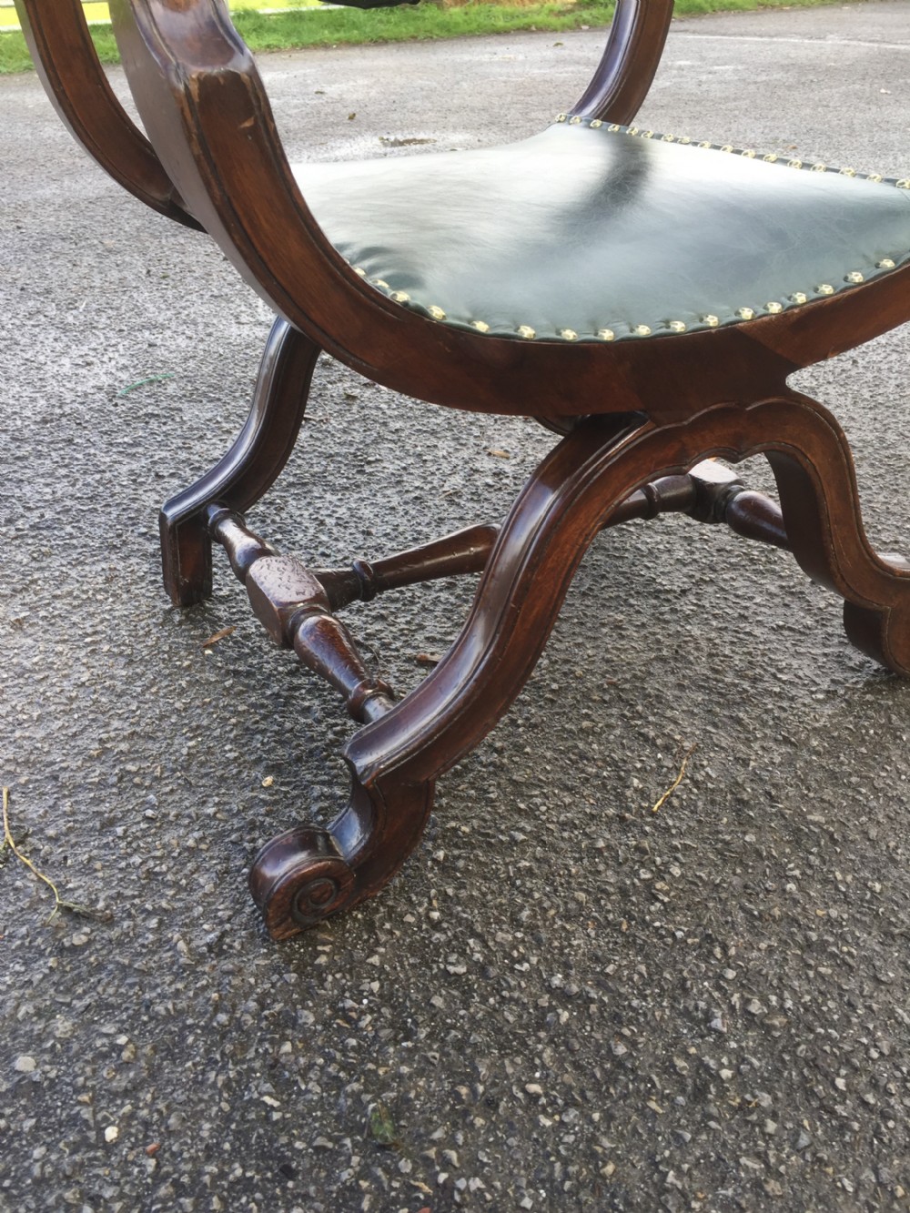 A nineteenth-century carved walnut X-frame armchair upholstered in dark olive green leather with brass stud details. View IV