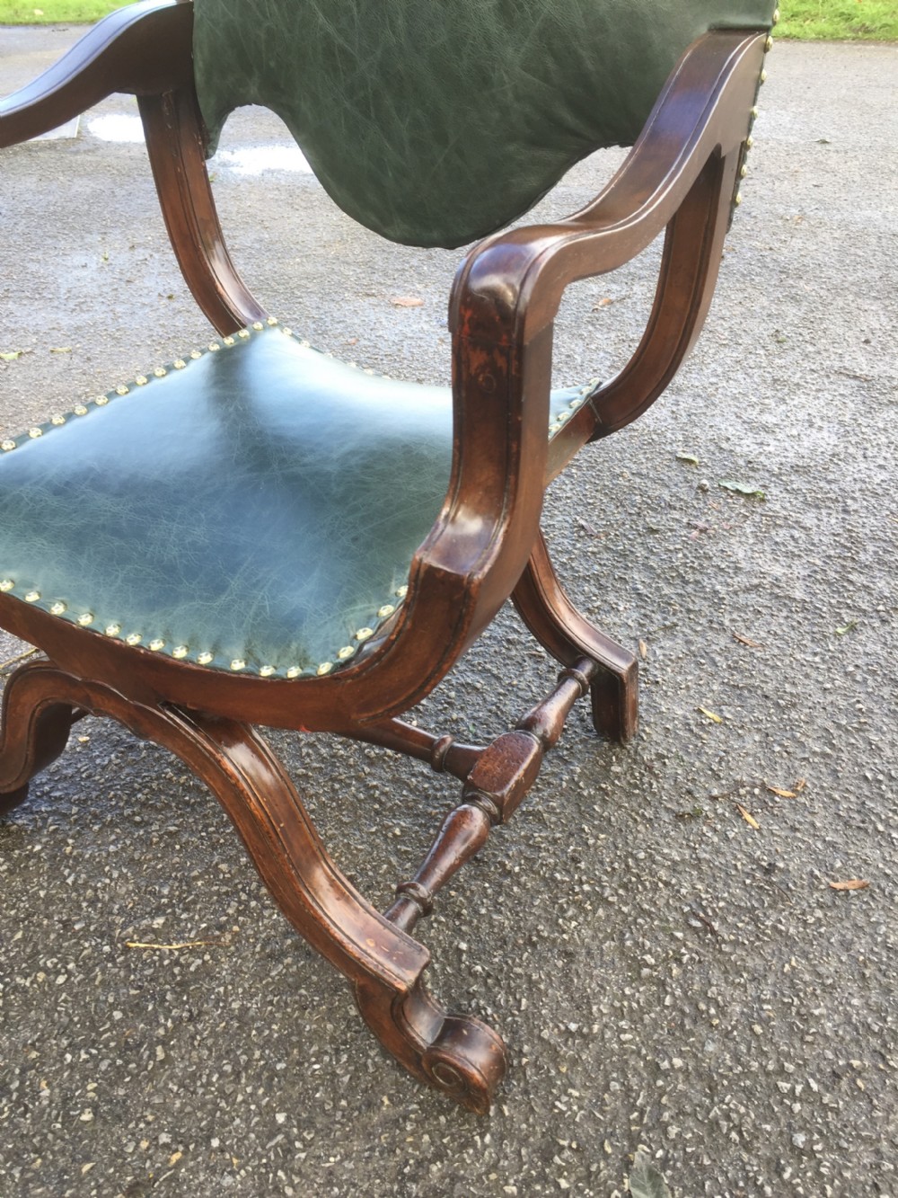 A nineteenth-century carved walnut X-frame armchair upholstered in dark olive green leather with brass stud details. View V