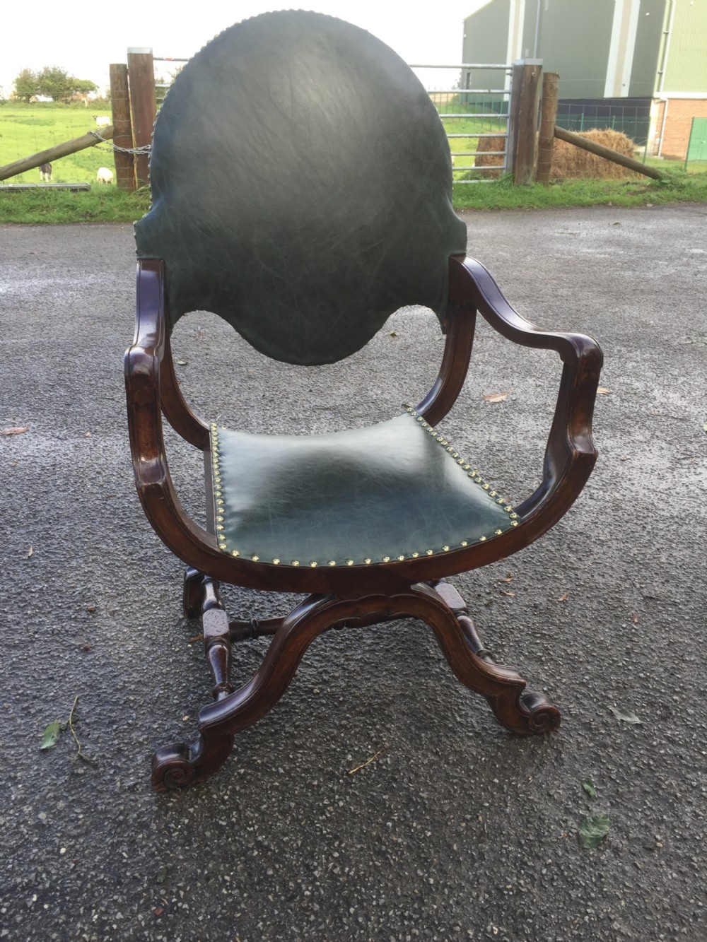 A nineteenth-century carved walnut X-frame armchair upholstered in dark olive green leather with brass stud details. View VI