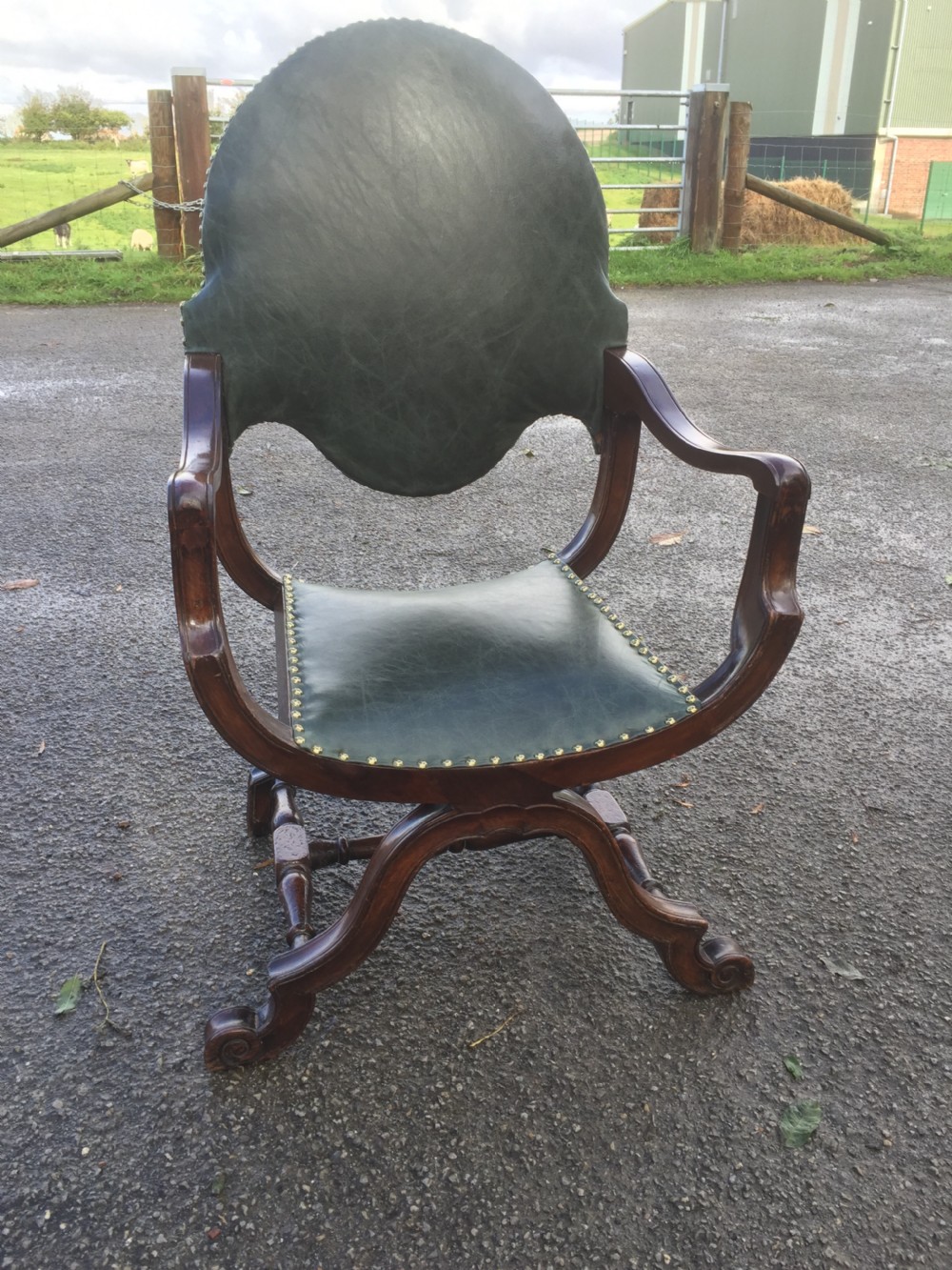 A nineteenth-century carved walnut X-frame armchair upholstered in dark olive green leather with brass stud details. View VII