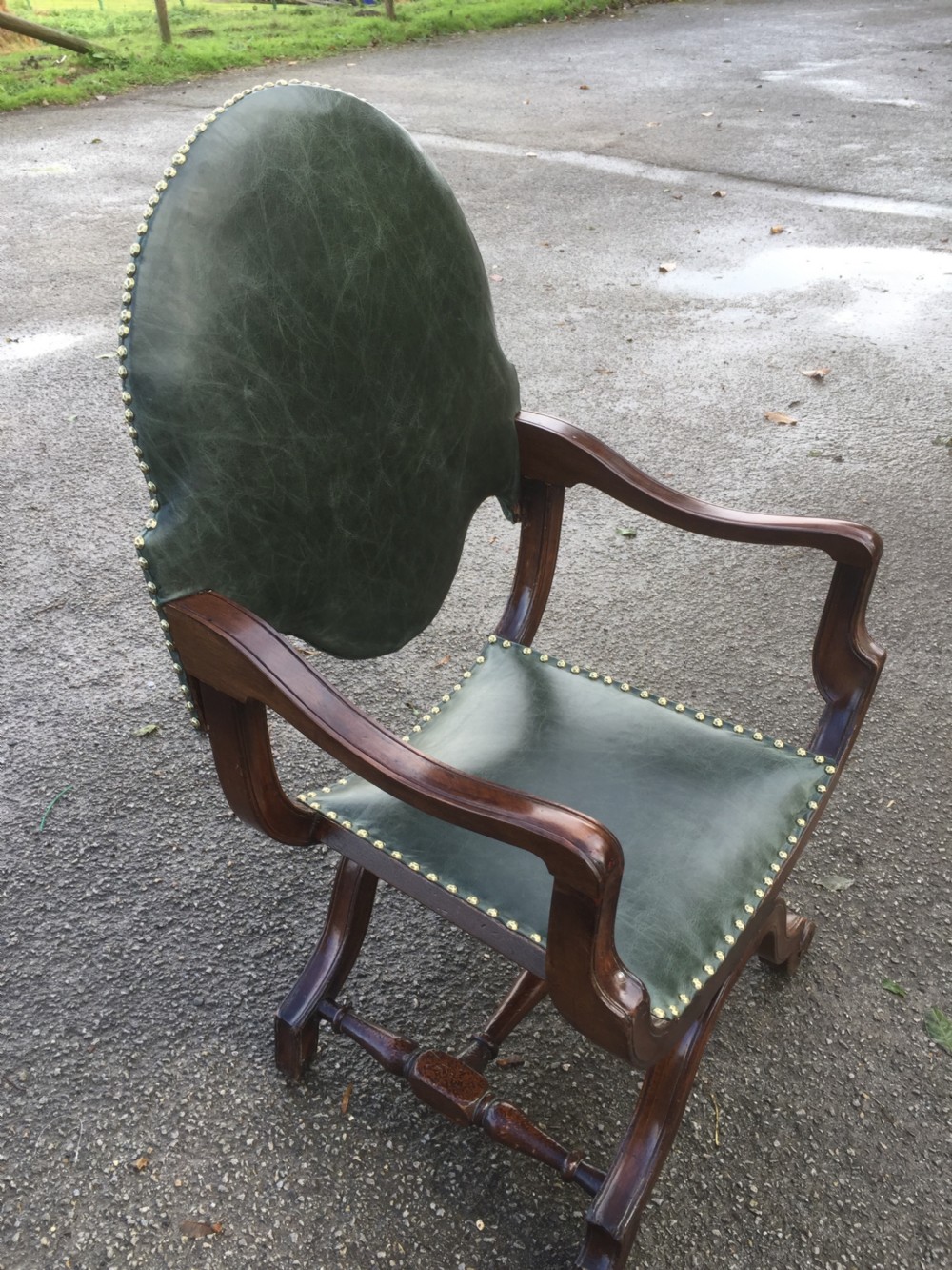A nineteenth-century carved walnut X-frame armchair upholstered in dark olive green leather with brass stud details. View IX