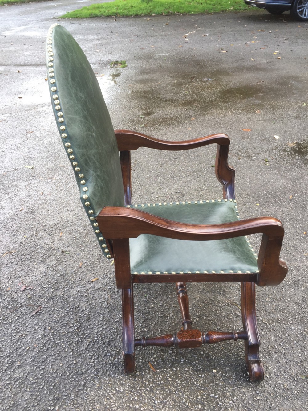 A nineteenth-century carved walnut X-frame armchair upholstered in dark olive green leather with brass stud details. View X