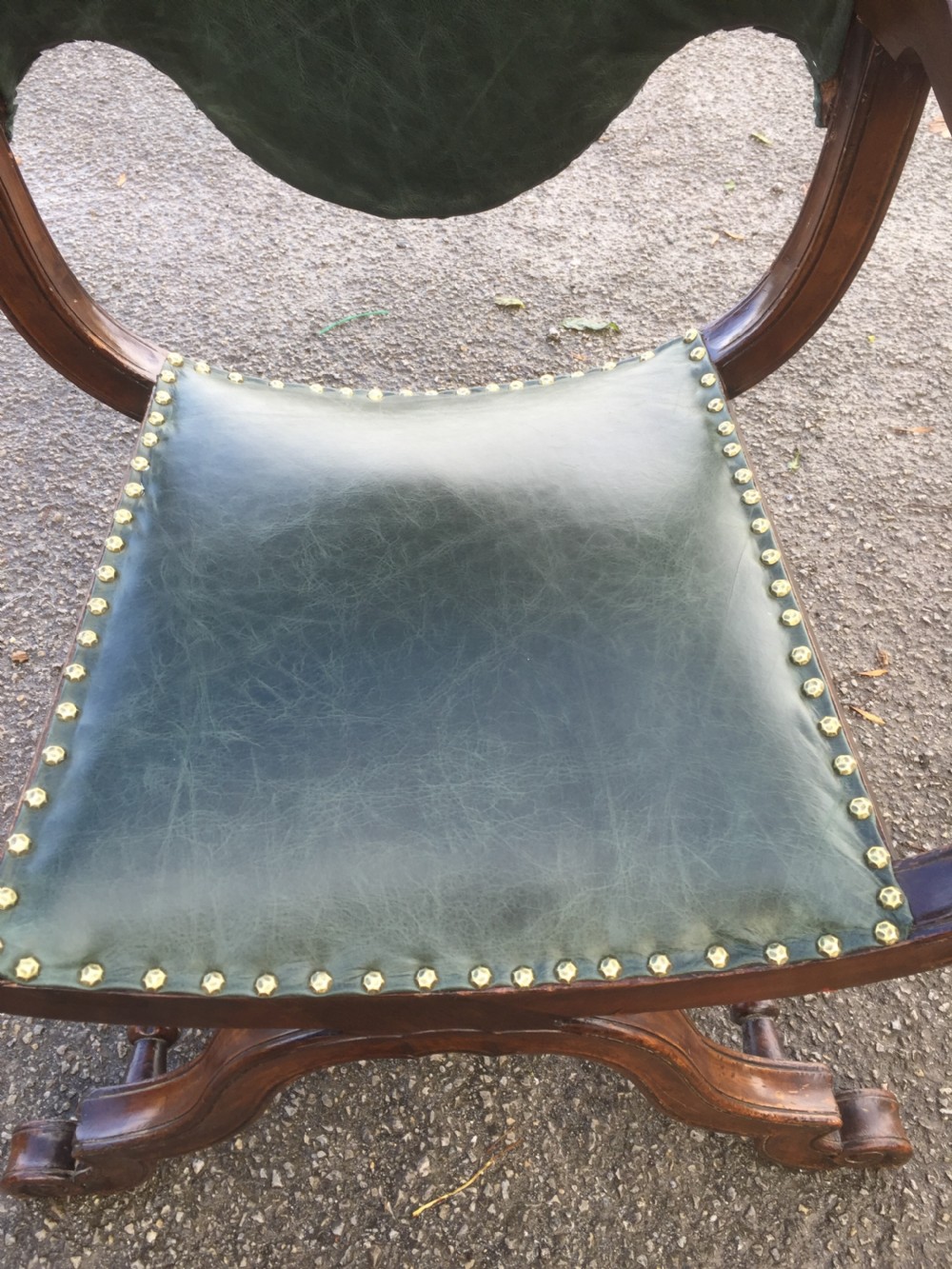 A nineteenth-century carved walnut X-frame armchair upholstered in dark olive green leather with brass stud details. View XII