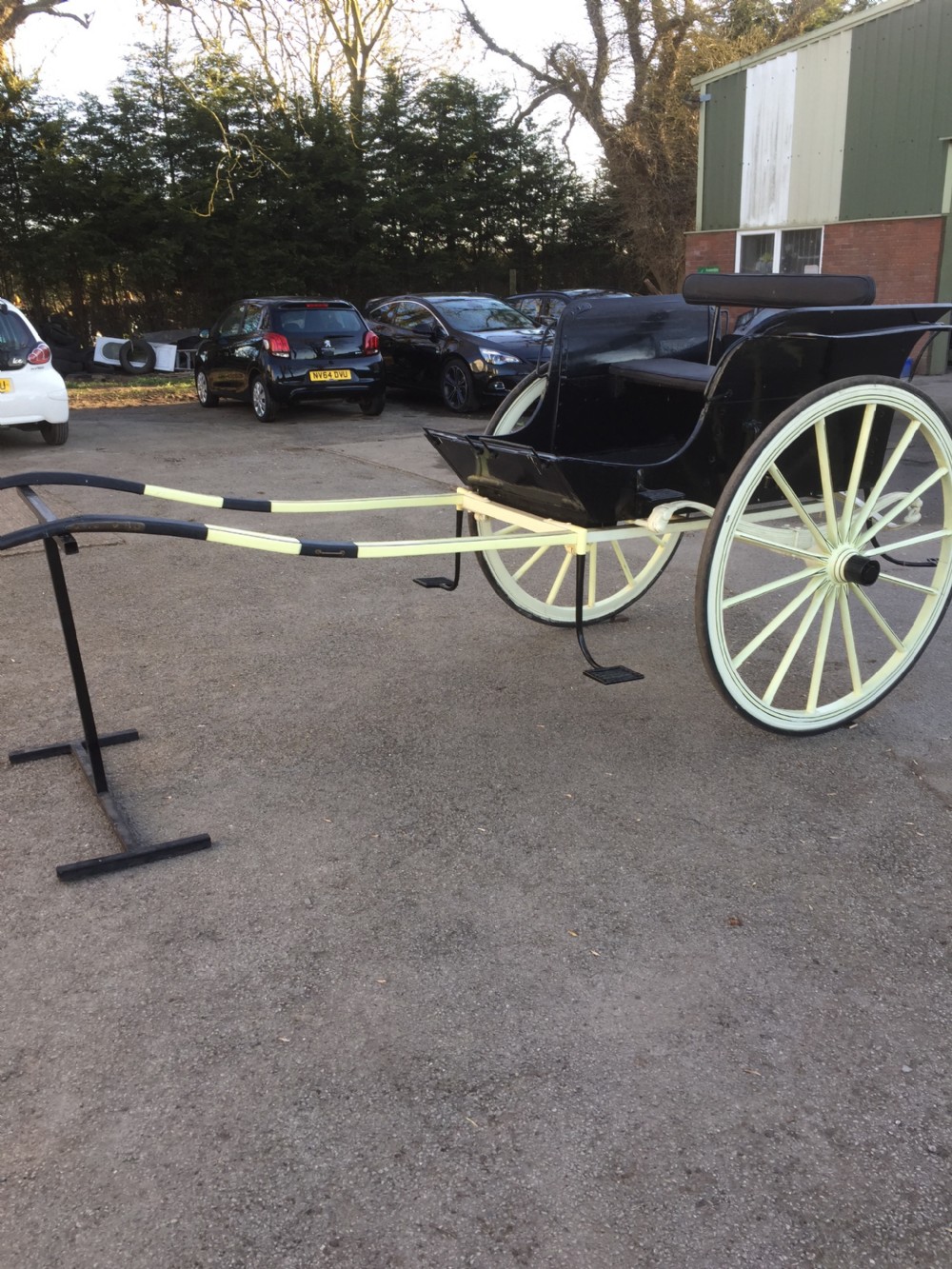 A nineteenth-century two-wheeled horse-drawn carriage featuring a black painted wooden body, cream spoked wheels, and extended shafts.