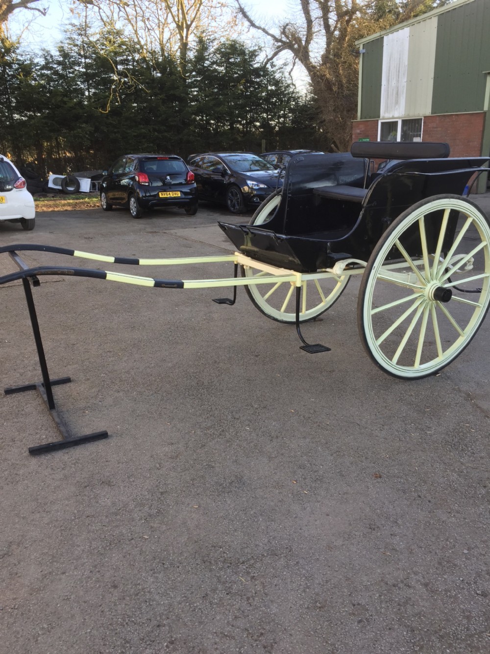 A nineteenth-century two-wheeled horse-drawn carriage featuring a black painted wooden body, cream spoked wheels, and extended shafts. View II