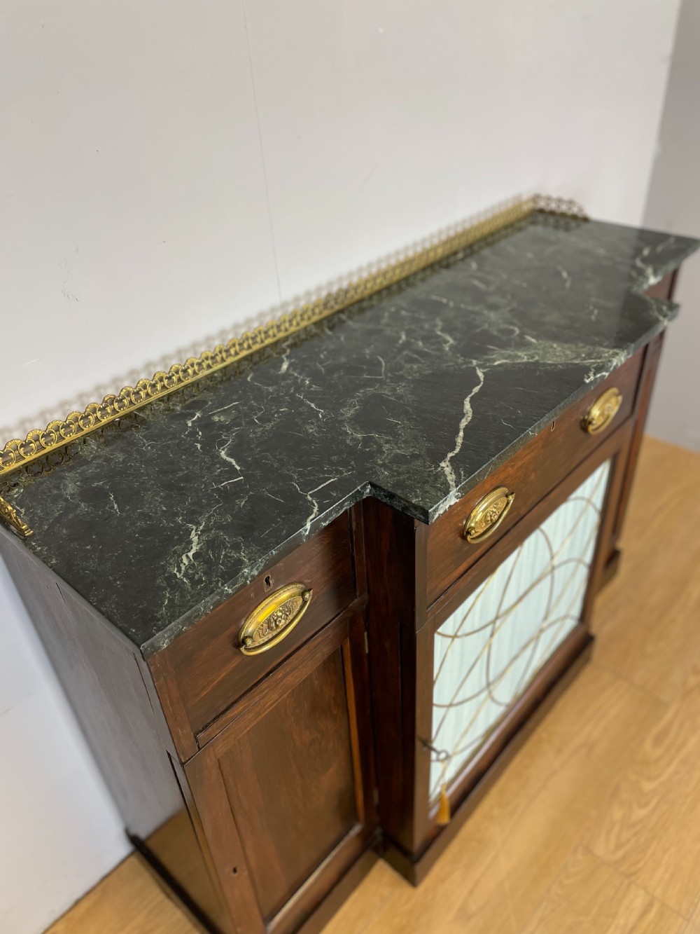 An early nineteenth-century Regency rosewood secretaire side cabinet featuring a dark green marble top with a brass gallery, a pleated fabric door panel, and brass handles. View V