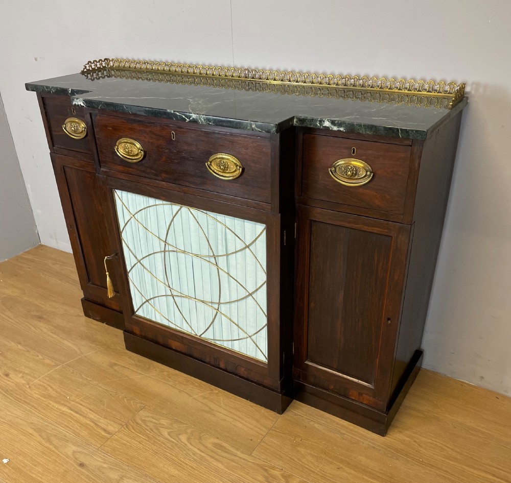 An early nineteenth-century Regency rosewood secretaire side cabinet featuring a dark green marble top with a brass gallery, a pleated fabric door panel, and brass handles. View VI