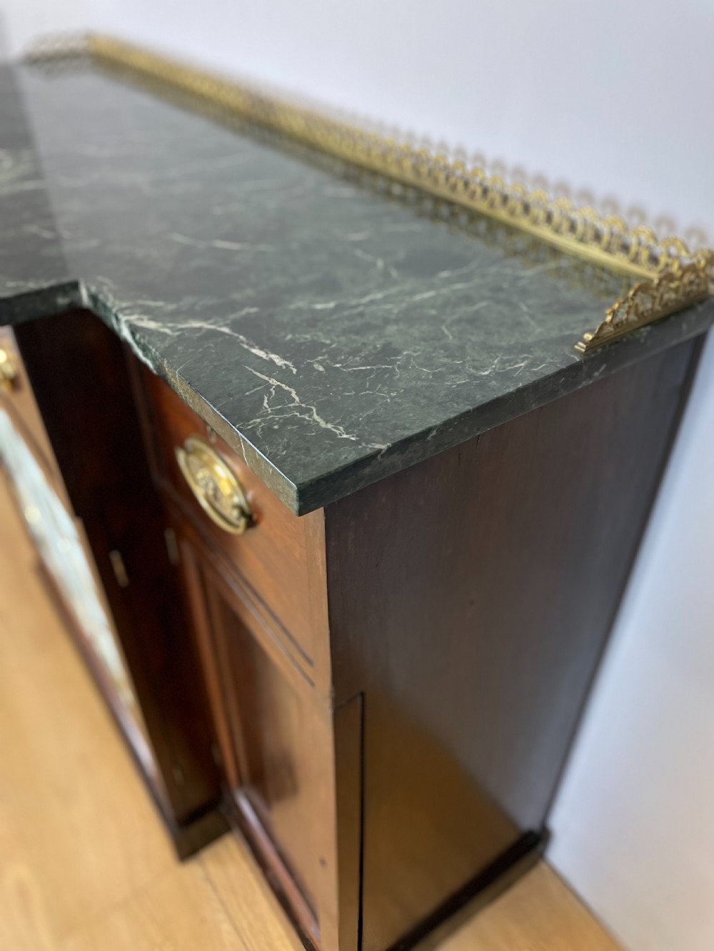 An early nineteenth-century Regency rosewood secretaire side cabinet featuring a dark green marble top with a brass gallery, a pleated fabric door panel, and brass handles. View VII