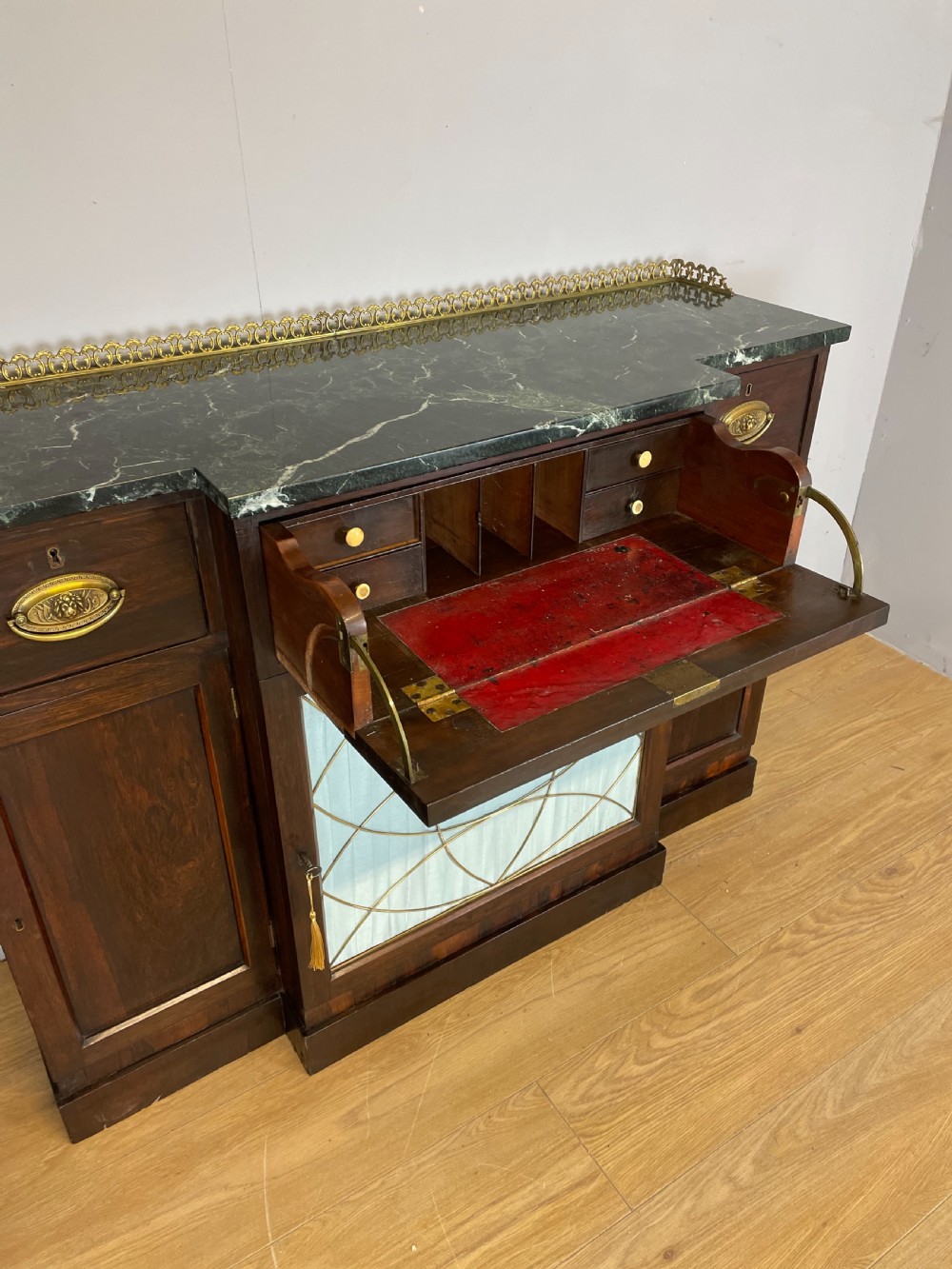 An early nineteenth-century Regency rosewood secretaire side cabinet featuring a dark green marble top with a brass gallery, a pleated fabric door panel, and brass handles. View VIII