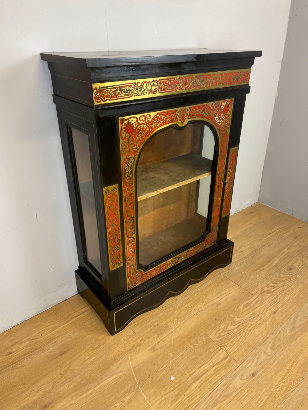 An ebonised nineteenth-century single-door display cabinet featuring brass and red tortoiseshell Boulle marquetry inlay around a glazed door and side panels.