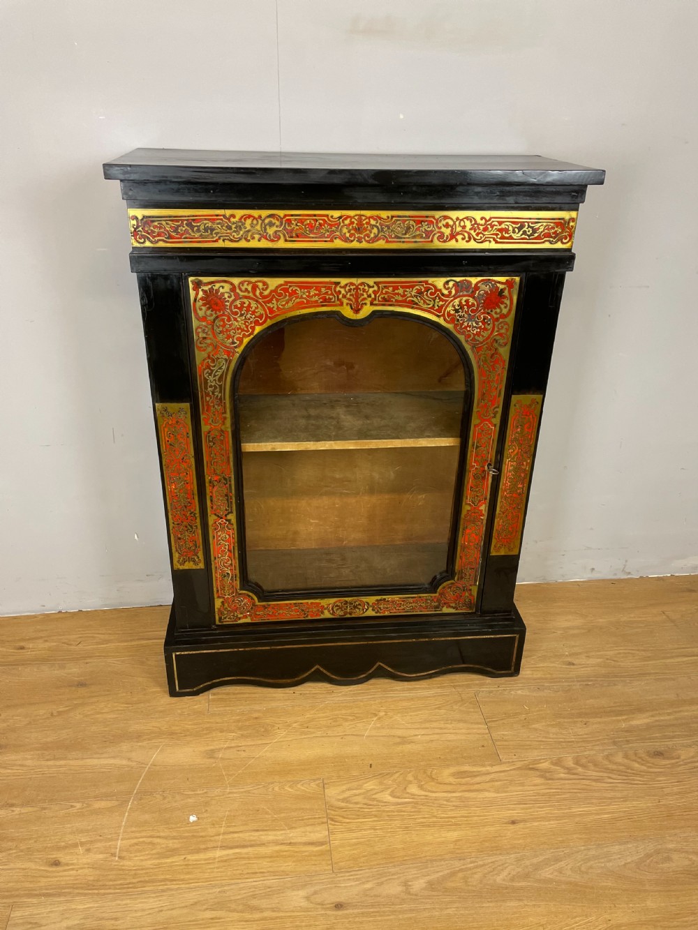 An ebonised nineteenth-century single-door display cabinet featuring brass and red tortoiseshell Boulle marquetry inlay around a glazed door and side panels. View II