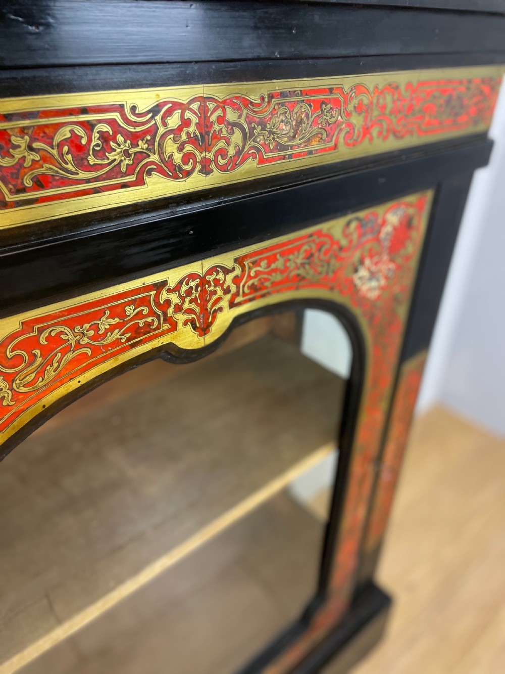 An ebonised nineteenth-century single-door display cabinet featuring brass and red tortoiseshell Boulle marquetry inlay around a glazed door and side panels. View IV