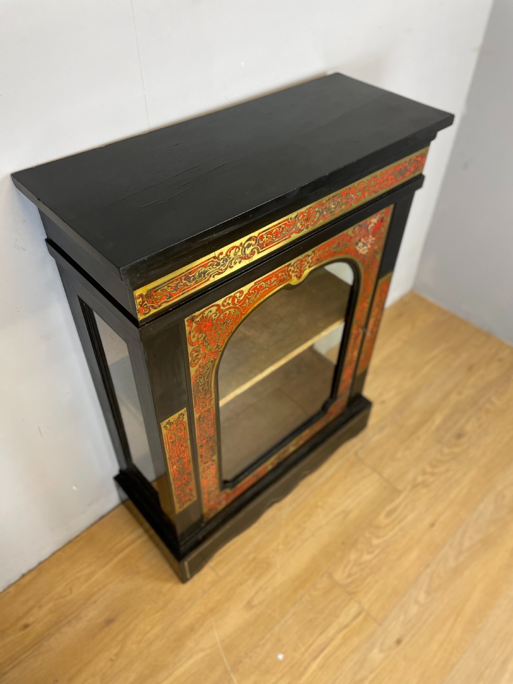 An ebonised nineteenth-century single-door display cabinet featuring brass and red tortoiseshell Boulle marquetry inlay around a glazed door and side panels. View V