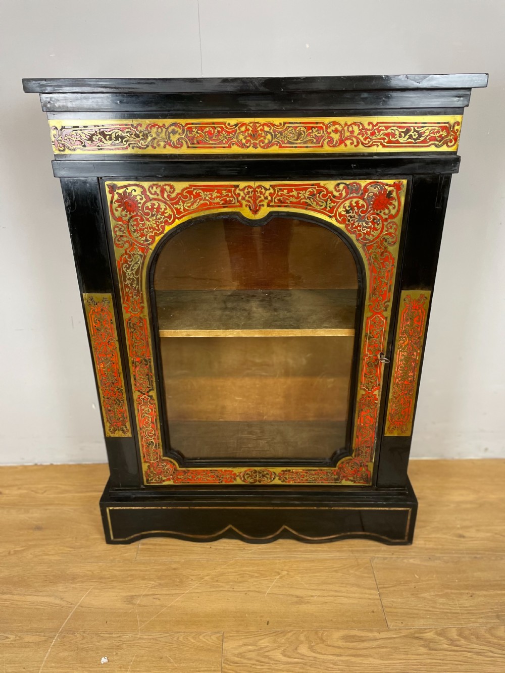An ebonised nineteenth-century single-door display cabinet featuring brass and red tortoiseshell Boulle marquetry inlay around a glazed door and side panels. View VI