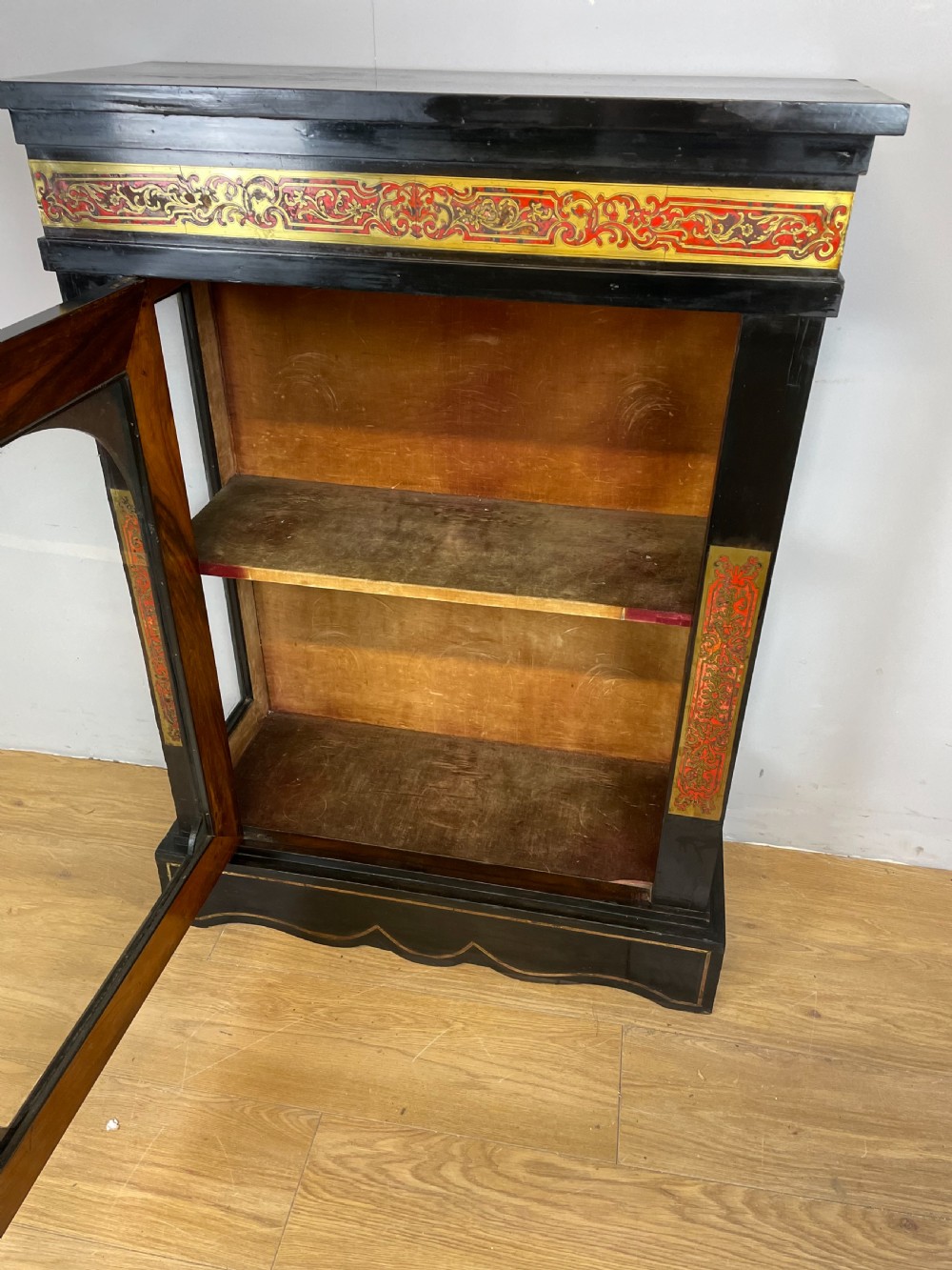 An ebonised nineteenth-century single-door display cabinet featuring brass and red tortoiseshell Boulle marquetry inlay around a glazed door and side panels. View VII