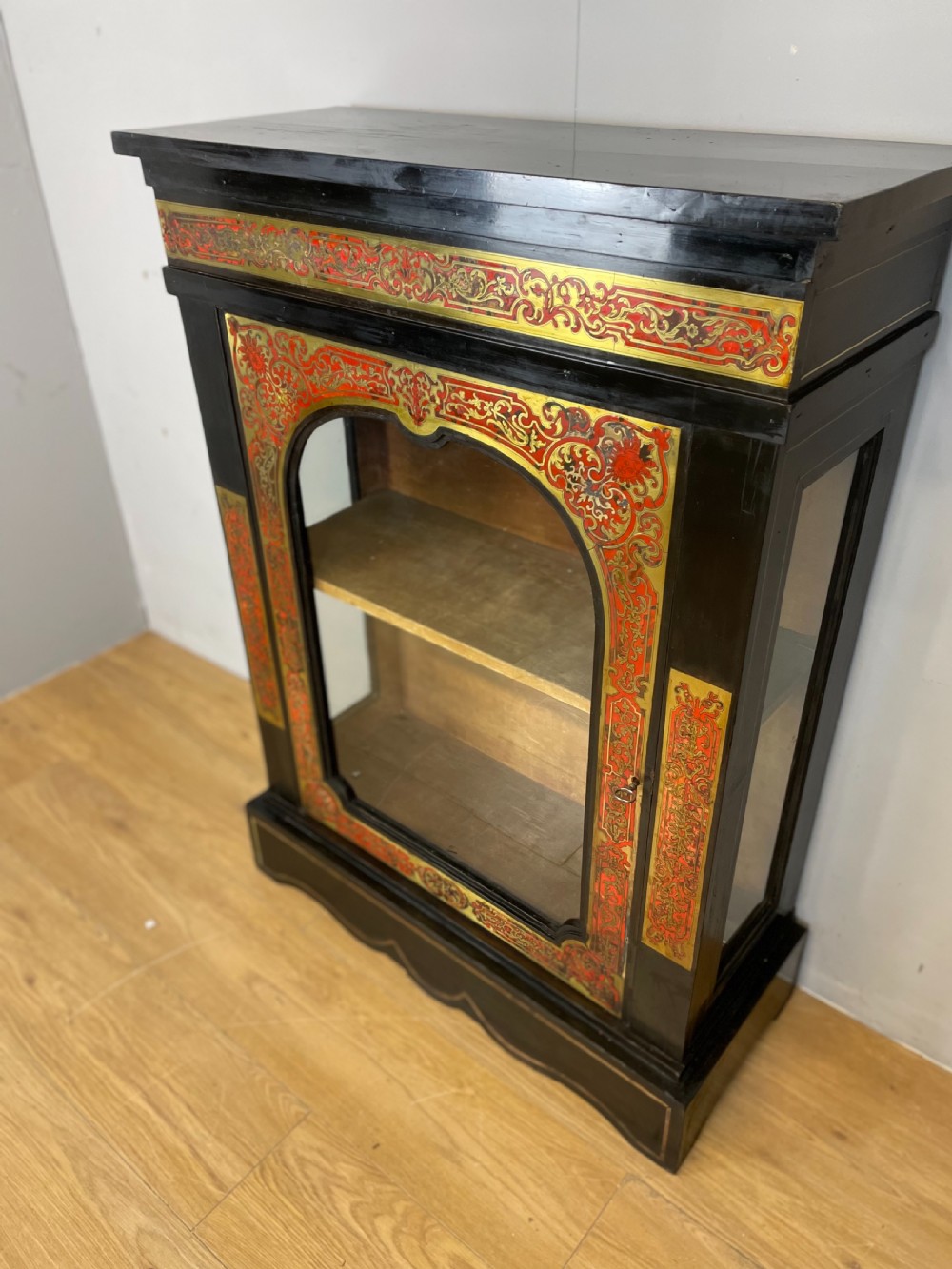 An ebonised nineteenth-century single-door display cabinet featuring brass and red tortoiseshell Boulle marquetry inlay around a glazed door and side panels. View X